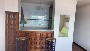 Una cocina compacta con un armario de madera, dos taburetes, una lámpara colgante y un salpicadero con diseño.