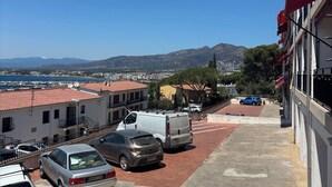 A parking area with several cars, a building with red awnings, and a view of distant mountains and a marina. - Apartment with a dream view in a prime location - Roses (Roses)