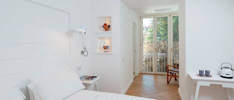 Un dormitorio moderno con una cama grande, una mesita de noche con hervidor y vistas a un balcón.