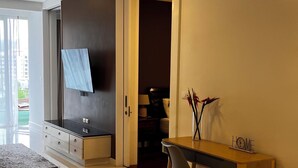 A modern living room with a flat-screen TV mounted on the wall, a wooden dining table with a chair, and a large window offering a view of the outdoors. - 2-bedroom apartment 127м² with a balcony 300m from the sea (Tambon Karon)