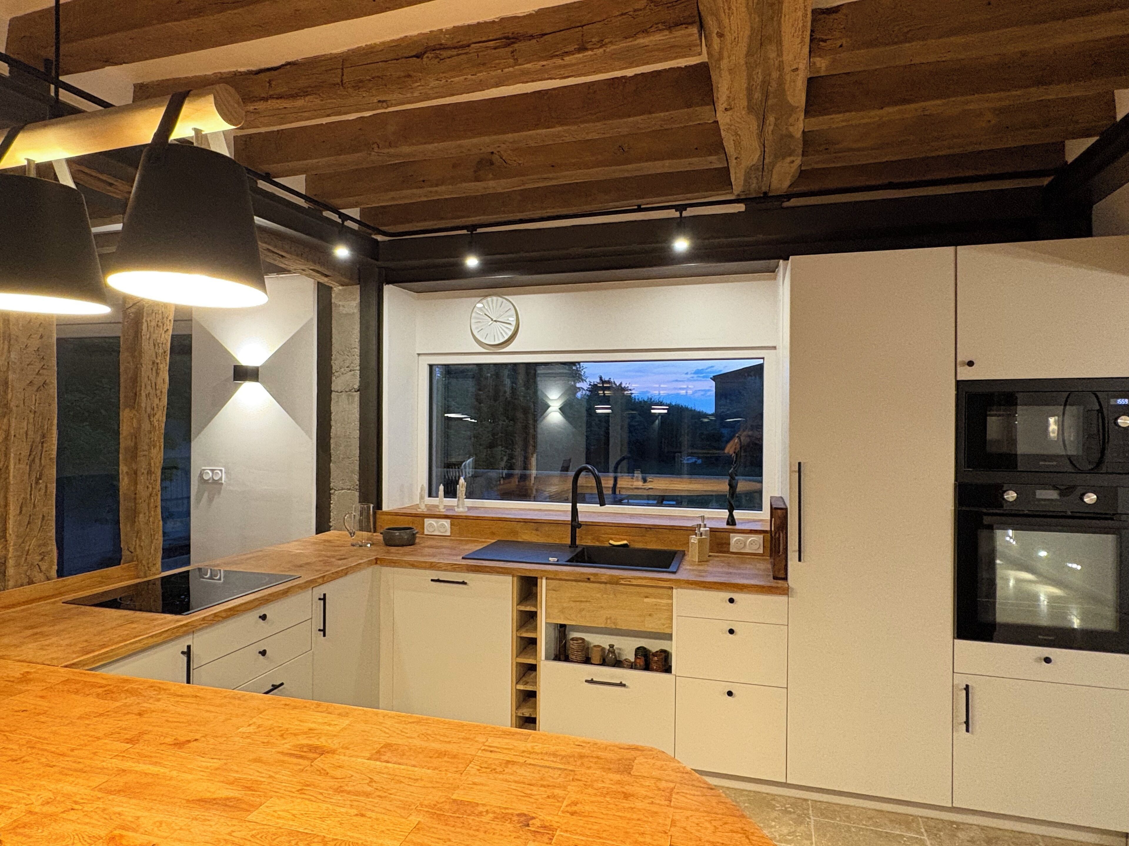 A modern kitchen with wooden beams, a large window, and built-in appliances.