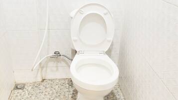 Des toilettes avec un abattant et un couvercle blancs, une commande de chasse d’eau fixée au mur et un sol orné d’un motif de petits galets.