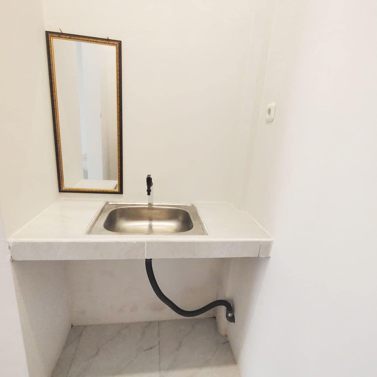 Une petite salle de bain avec un lavabo blanc, un miroir et un tuyau noir.