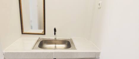 Une petite salle de bain avec un lavabo blanc, un miroir et un tuyau noir.
