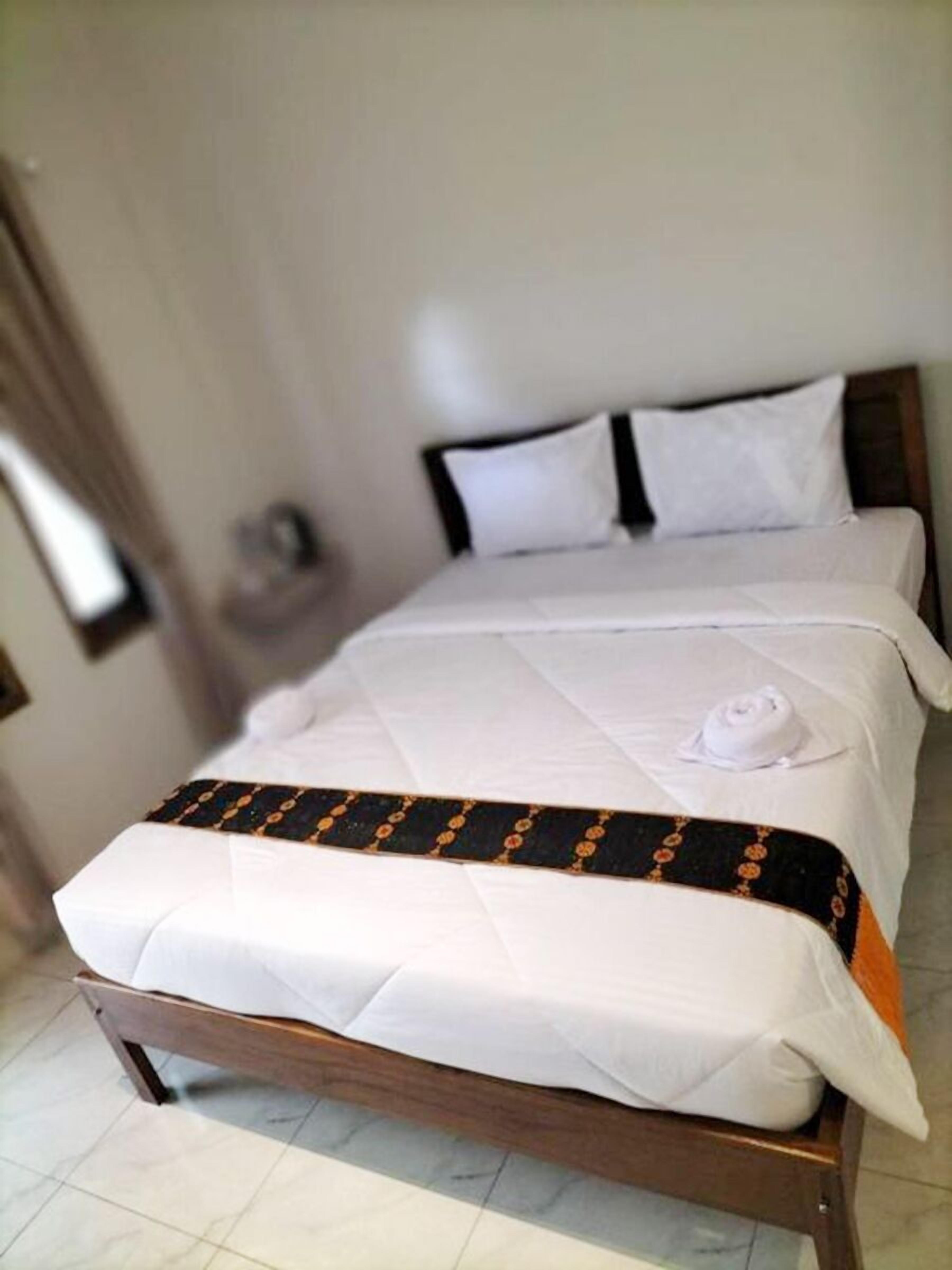 Een net opgemaakt bed met witte lakens en een zwart-oranje decoratiedeken.