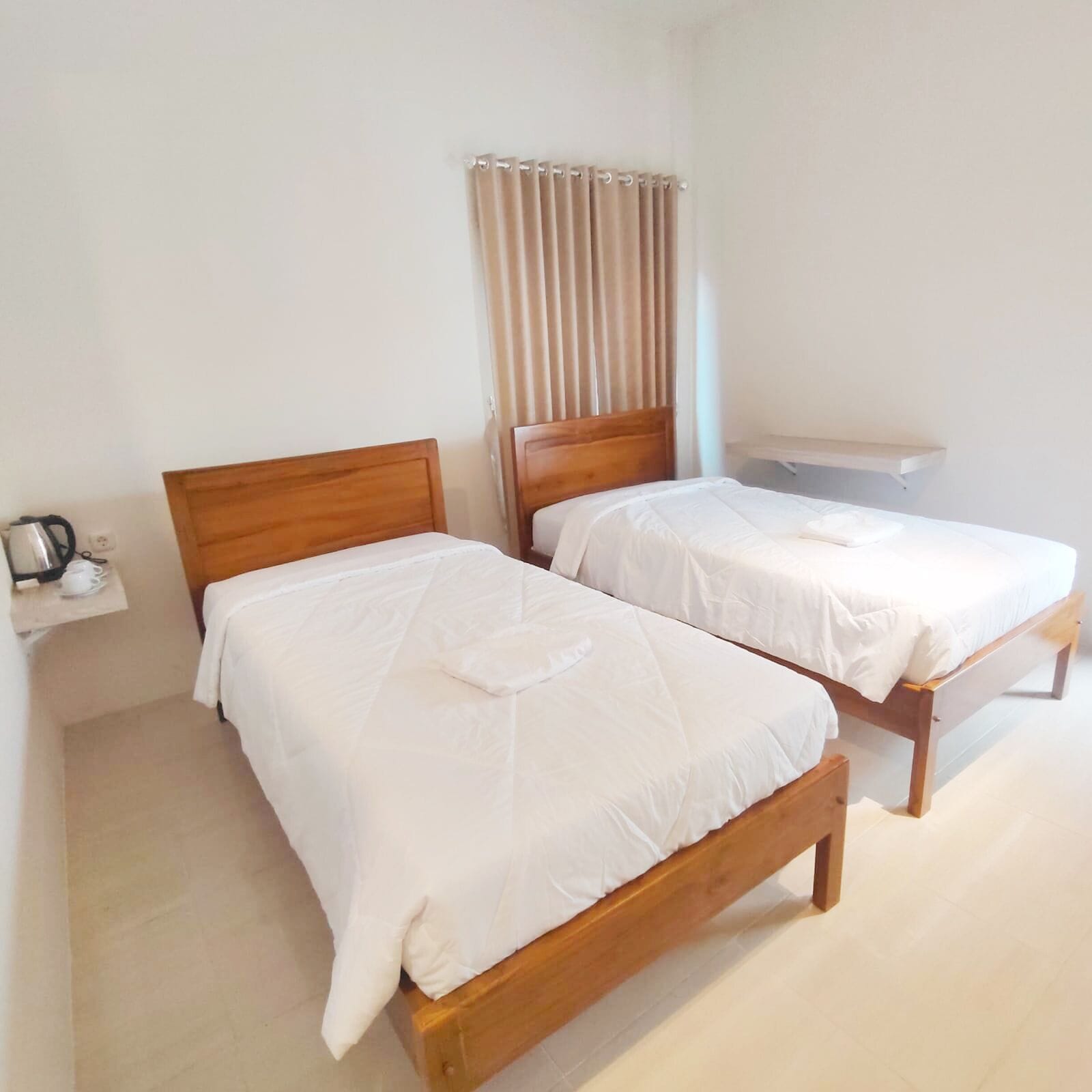 Habitación de hotel con dos camas de madera, una mesita con hervidor y una ventana con cortinas.