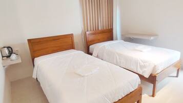 Habitación de hotel con dos camas de madera, una mesita con hervidor y una ventana con cortinas.