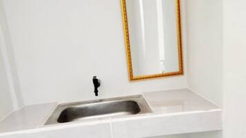 Une salle de bain avec un lavabo blanc, un miroir avec un cadre doré et une poubelle verte.