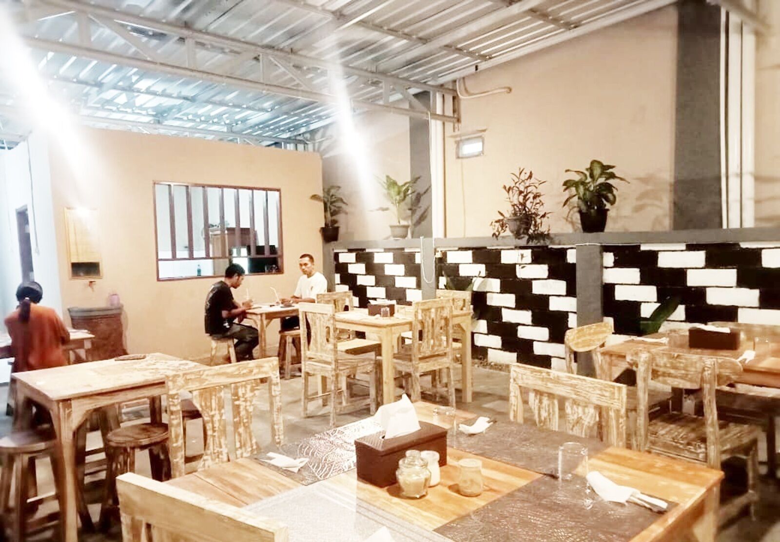 Un restaurant avec des meubles en bois, un mur orné d’un motif noir et blanc et des plantes en pot.