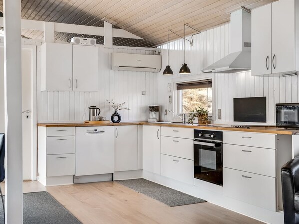 Una cocina moderna con armarios blancos, encimera de madera y horno empotrado.