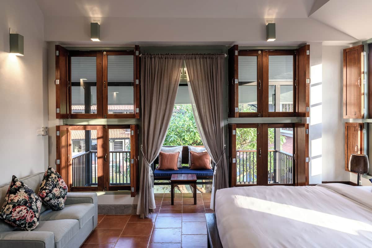 A bedroom with a large bed, a sofa with floral cushions, and a view of a balcony with a wooden railing.