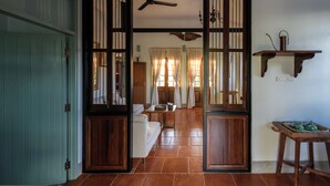 A traditional room with a wooden door, a ceiling fan, a sofa, and a table with a teapot. - Villa Pateh (Sikao)