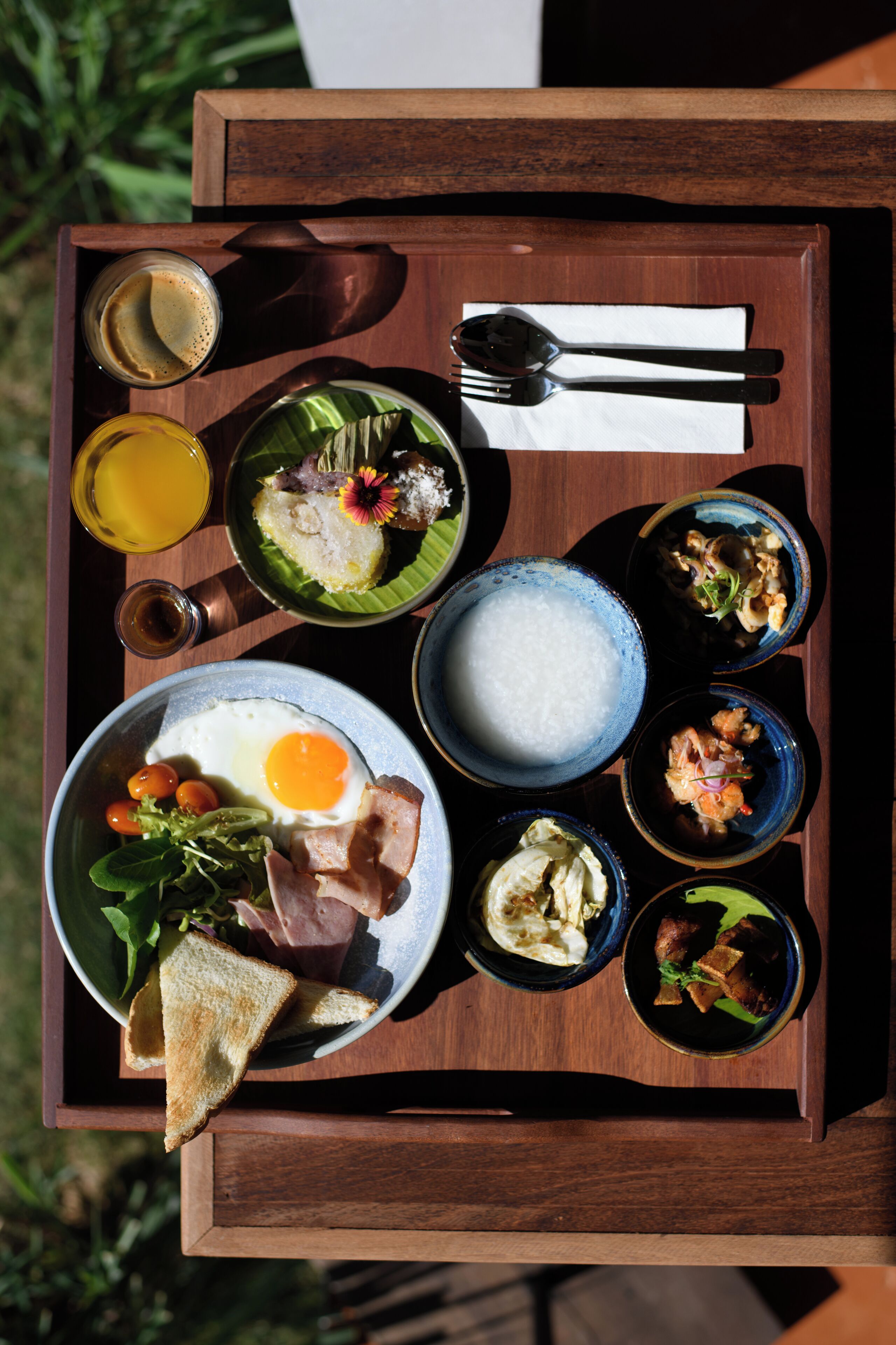 A wooden tray with a variety of breakfast items including eggs, toast, and several small bowls of food.