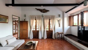 A living room with a sofa, a coffee table, and a television. There are curtains on the windows and a wooden beam on the ceiling. - Villa Pateh (Sikao)