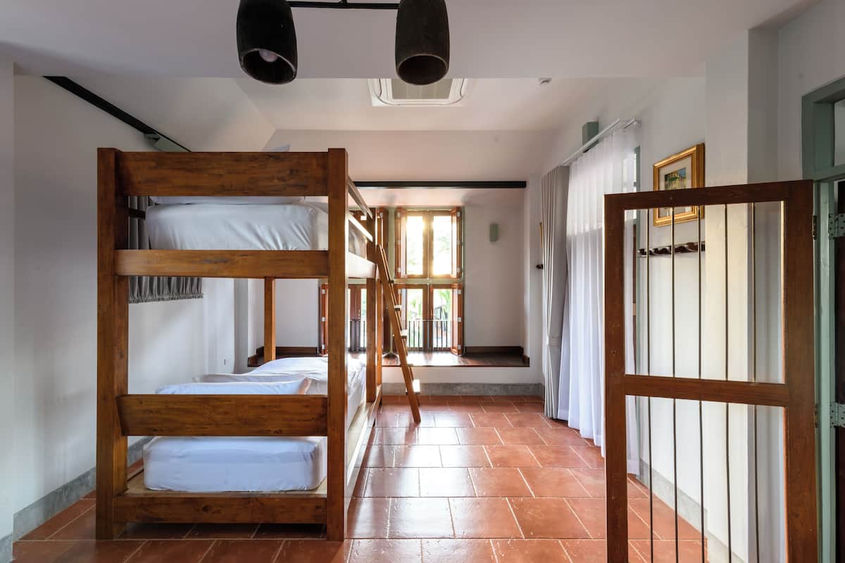 A dormitory room with bunk beds, a staircase, and a view of the outside.