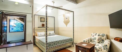 A bedroom with a four-poster bed, a chair, a small table, and a television on the wall.