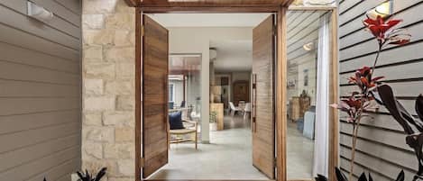 Puerta de madera que da a una sala de estar con pared de piedra, felpudo y planta.