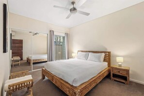 A bedroom with a large bed, a bedside table, a chair, a ceiling fan, and a sliding glass door leading to an outdoor area.