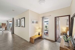 A hallway with a bench, framed pictures, a lamp, and a mirror. - Leeuwin House—Spacious Seaside Living for Groups (Quindalup)