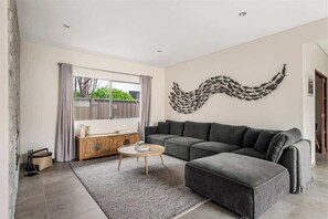Un salon moderne avec un canapé d’angle gris, une table basse ronde et un élément décoratif mural.