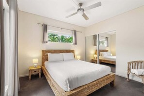 A bedroom with a wooden bed, a ceiling fan, a nightstand, a bench, and a large mirror. - Leeuwin House—Spacious Seaside Living for Groups (Quindalup)