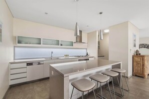 A modern kitchen with a central island, bar stools, and pendant lighting. - Leeuwin House—Spacious Seaside Living for Groups (Quindalup)