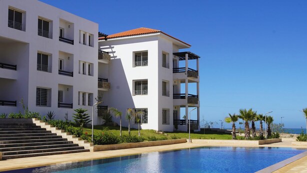 A modern multi-story building with a swimming pool in front.