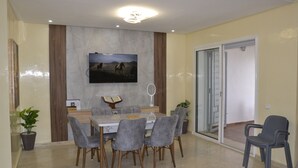 A dining area with a marble wall, a flat-screen TV, and a sliding glass door leading to a balcony.