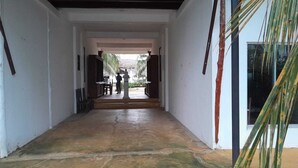 A corridor with a tiled floor leading to a courtyard with a statue and palm trees. - Mami Beach Resort (Tangalle)