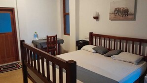 A bedroom with a wooden bed, a desk with a chair, a water bottle, and a picture on the wall. - Mami Beach Resort (Tangalle)