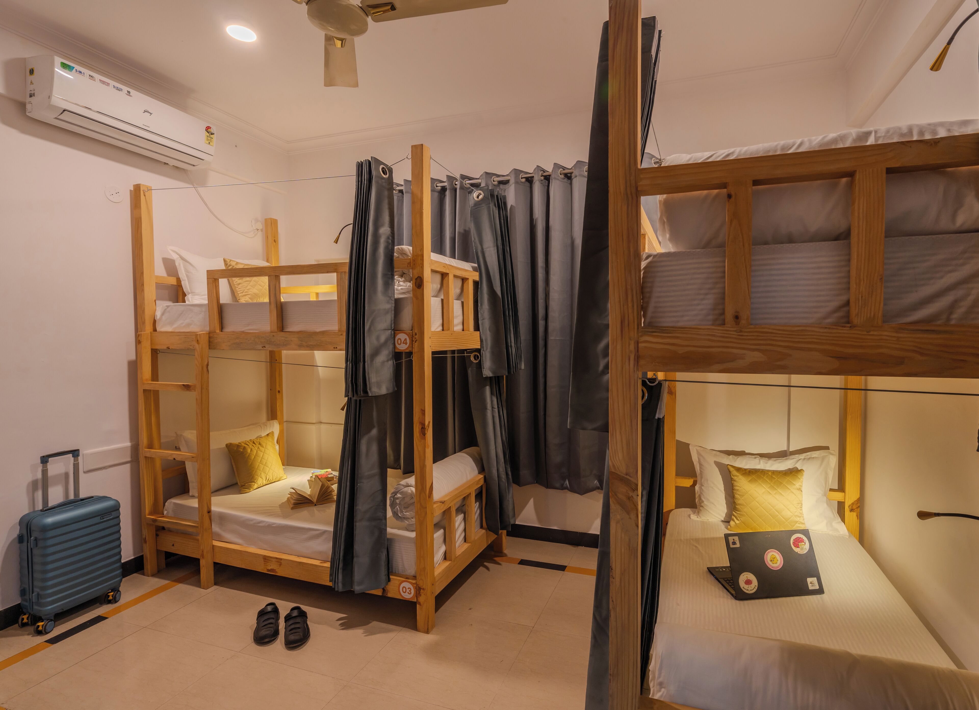 Une chambre de dortoir avec des lits superposés, une valise et un ordinateur portable posés sur le sol.