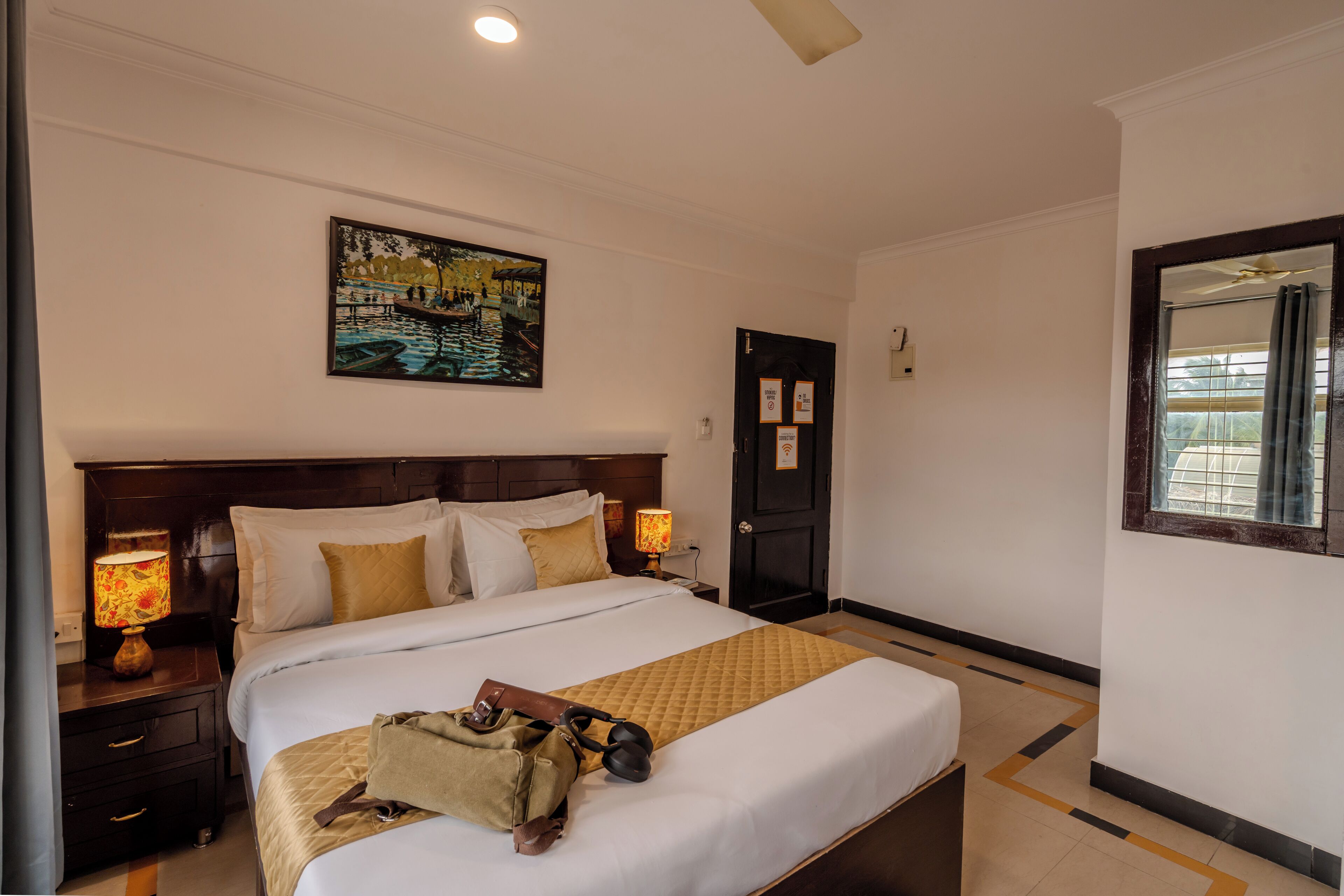 A neatly made bed with a quilt, a painting above it, and a nightstand with a lamp.