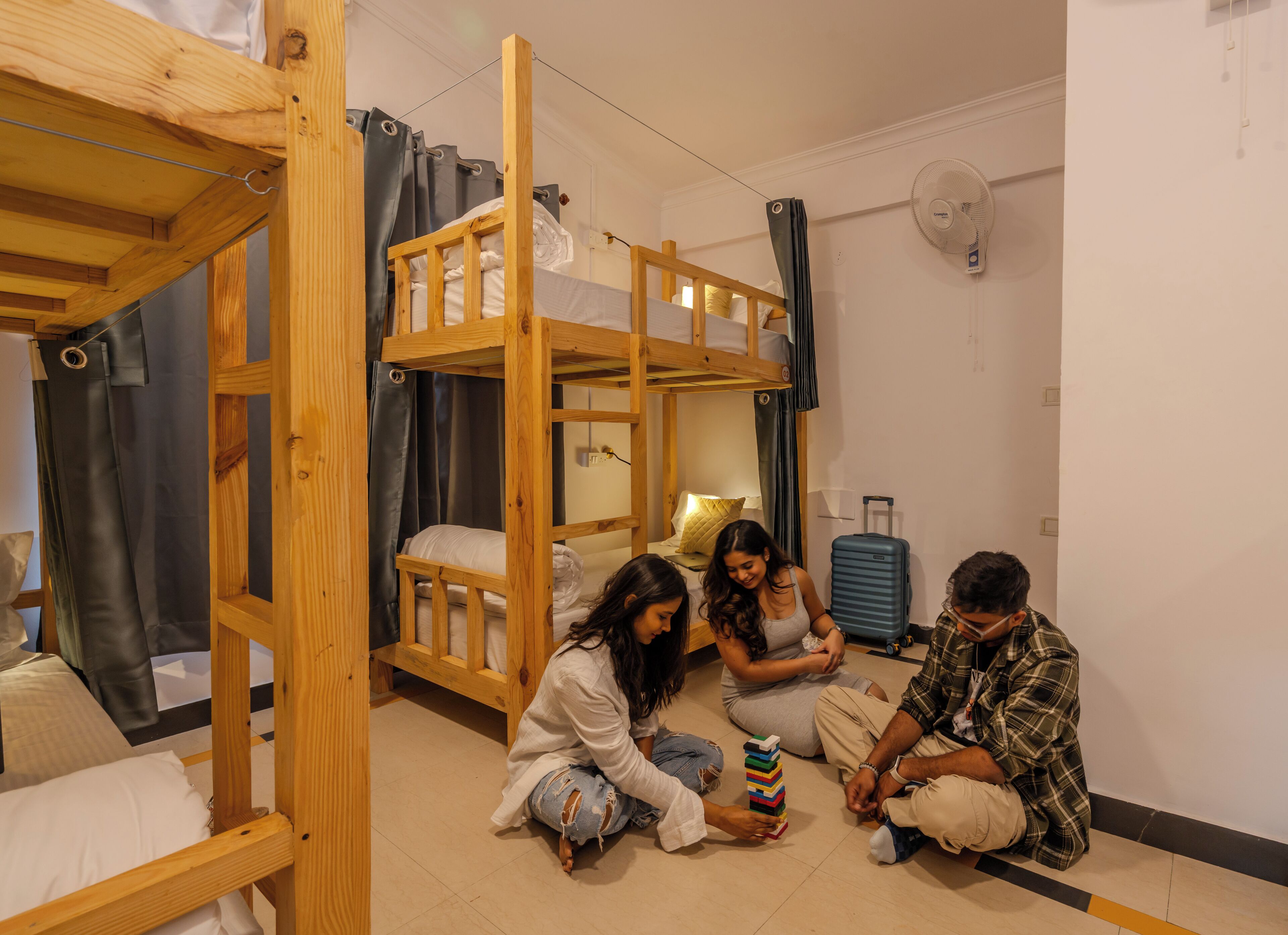 A room with bunk beds, a fan, and a suitcase.