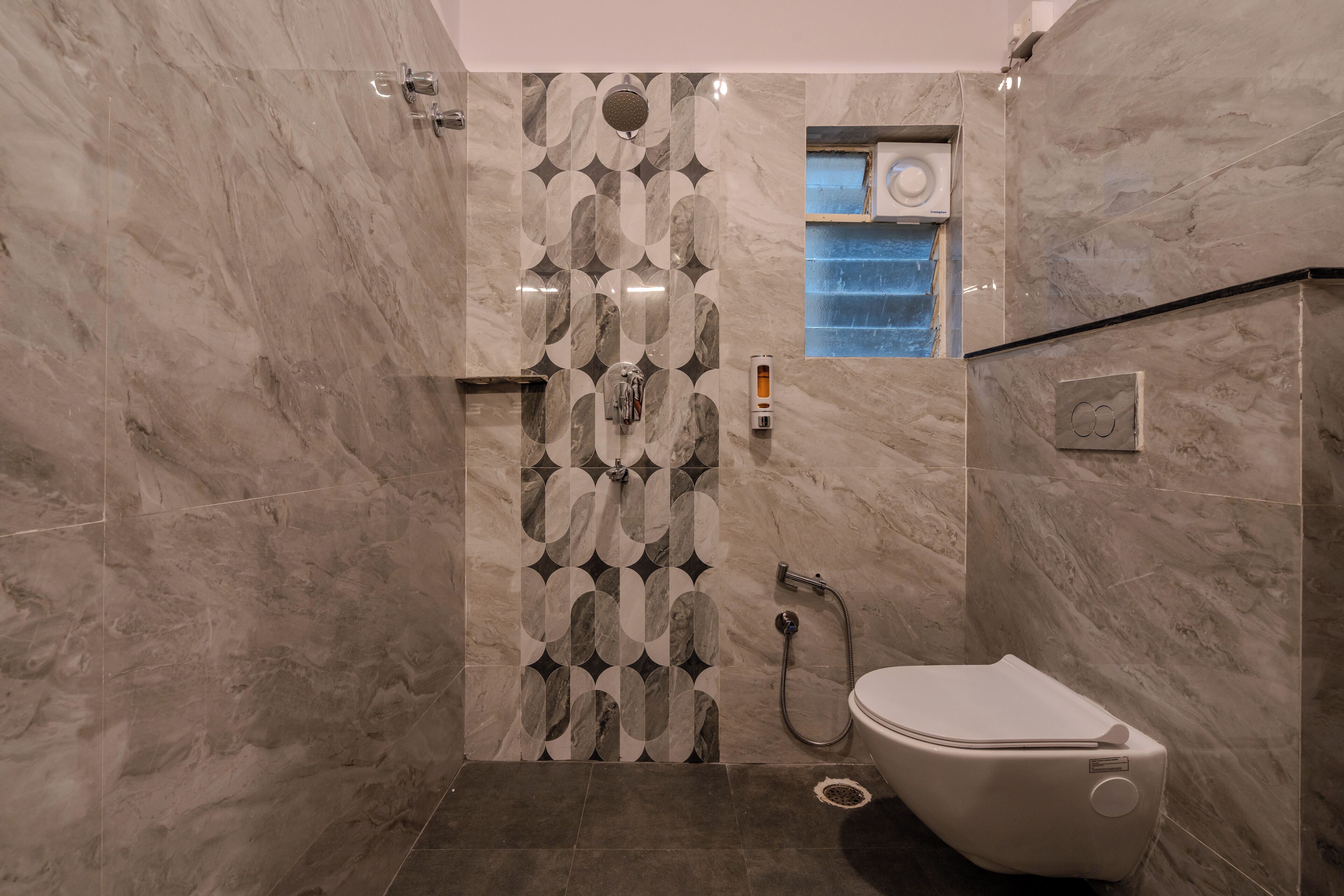 A bathroom with a marble wall, a shower, and a toilet.