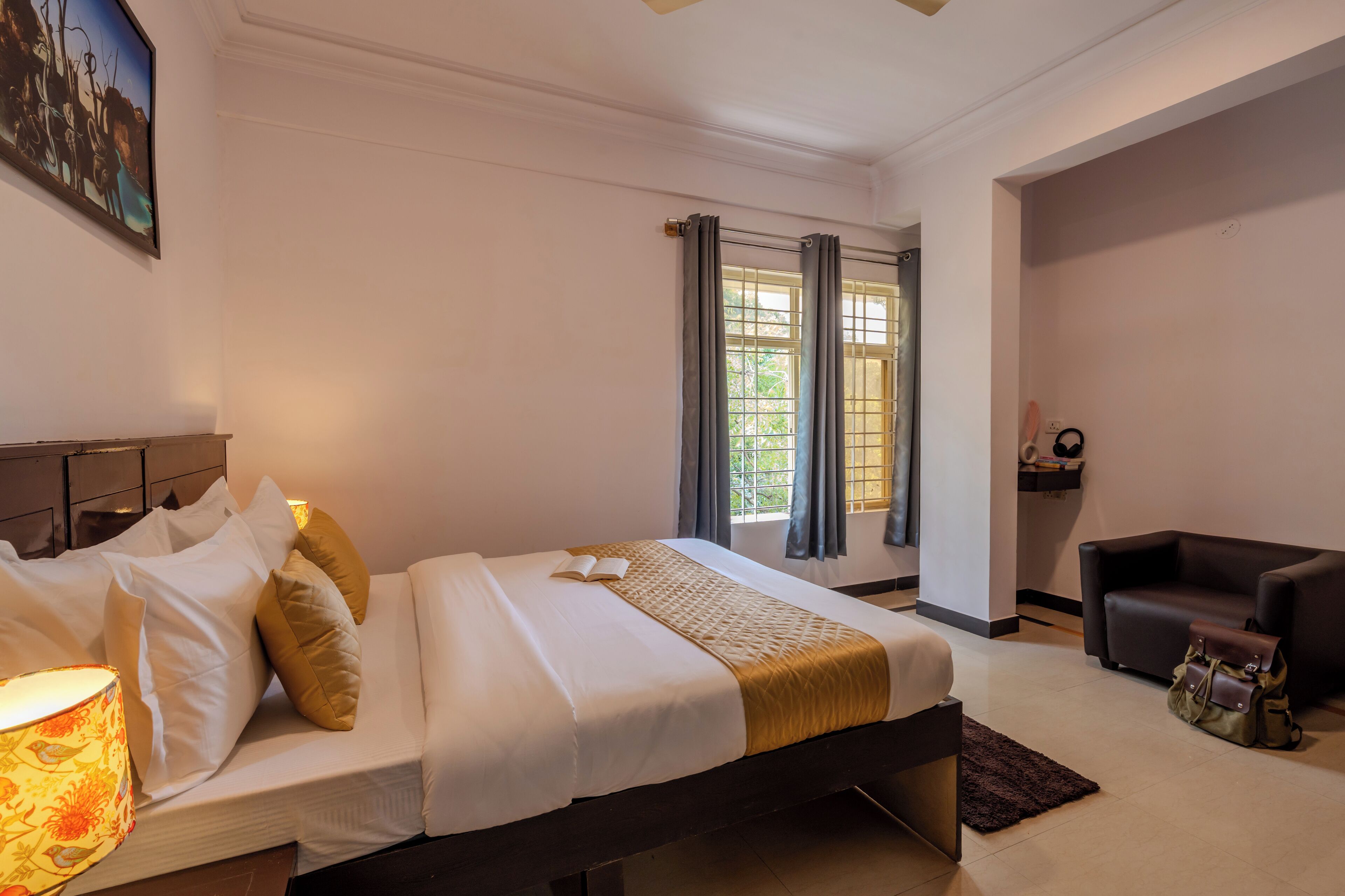 A hotel room with a bed, a chair, a lamp, and a window with curtains.