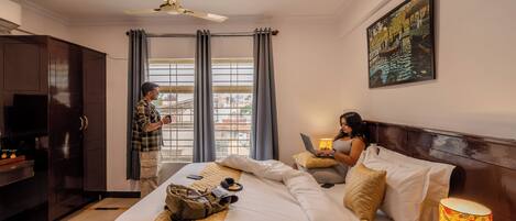 A hotel room with a bed, a desk, a TV, a ceiling fan, and a window with curtains.