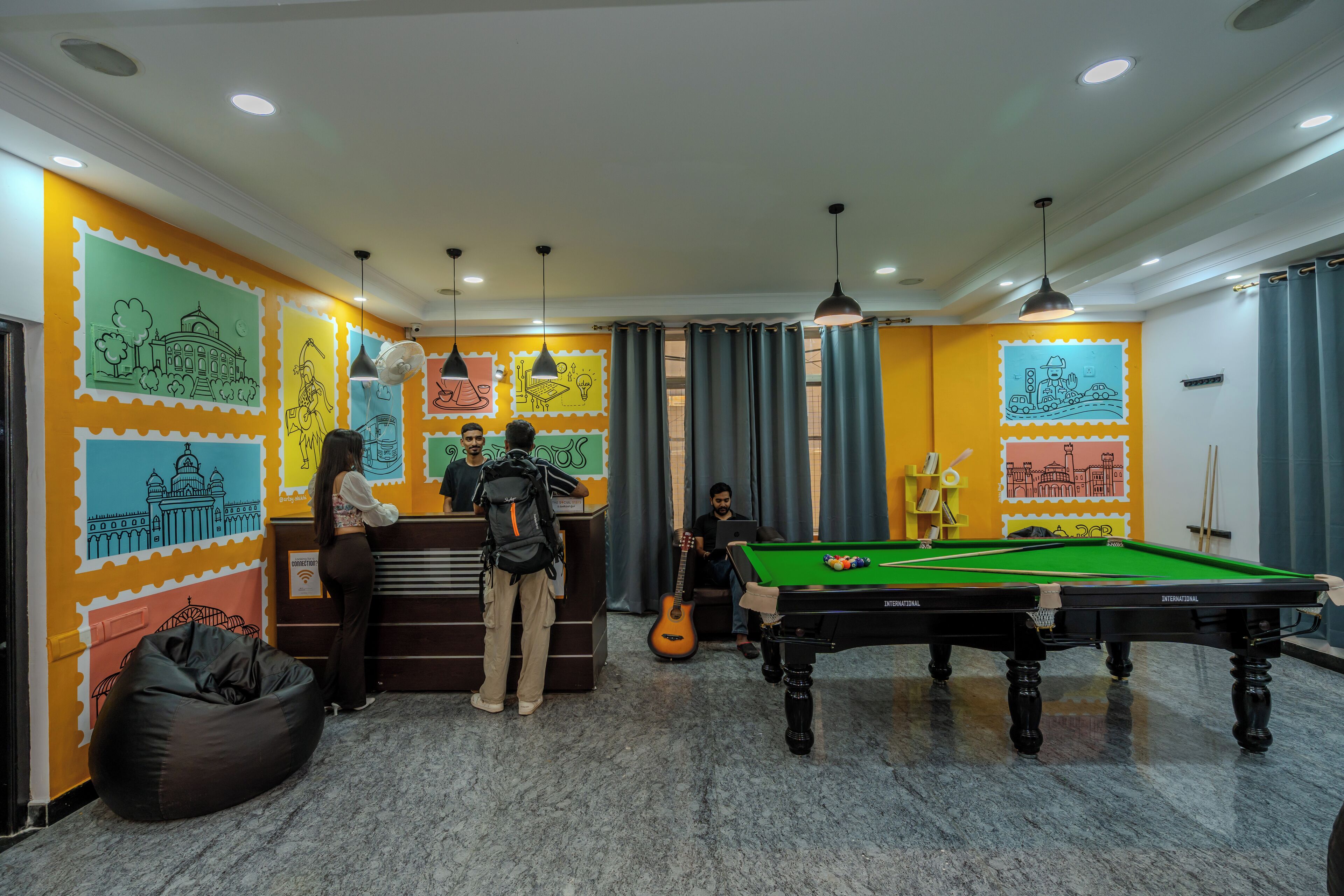 A pool table, a bean bag chair, and a person standing near a counter in a room with colorful wall art.