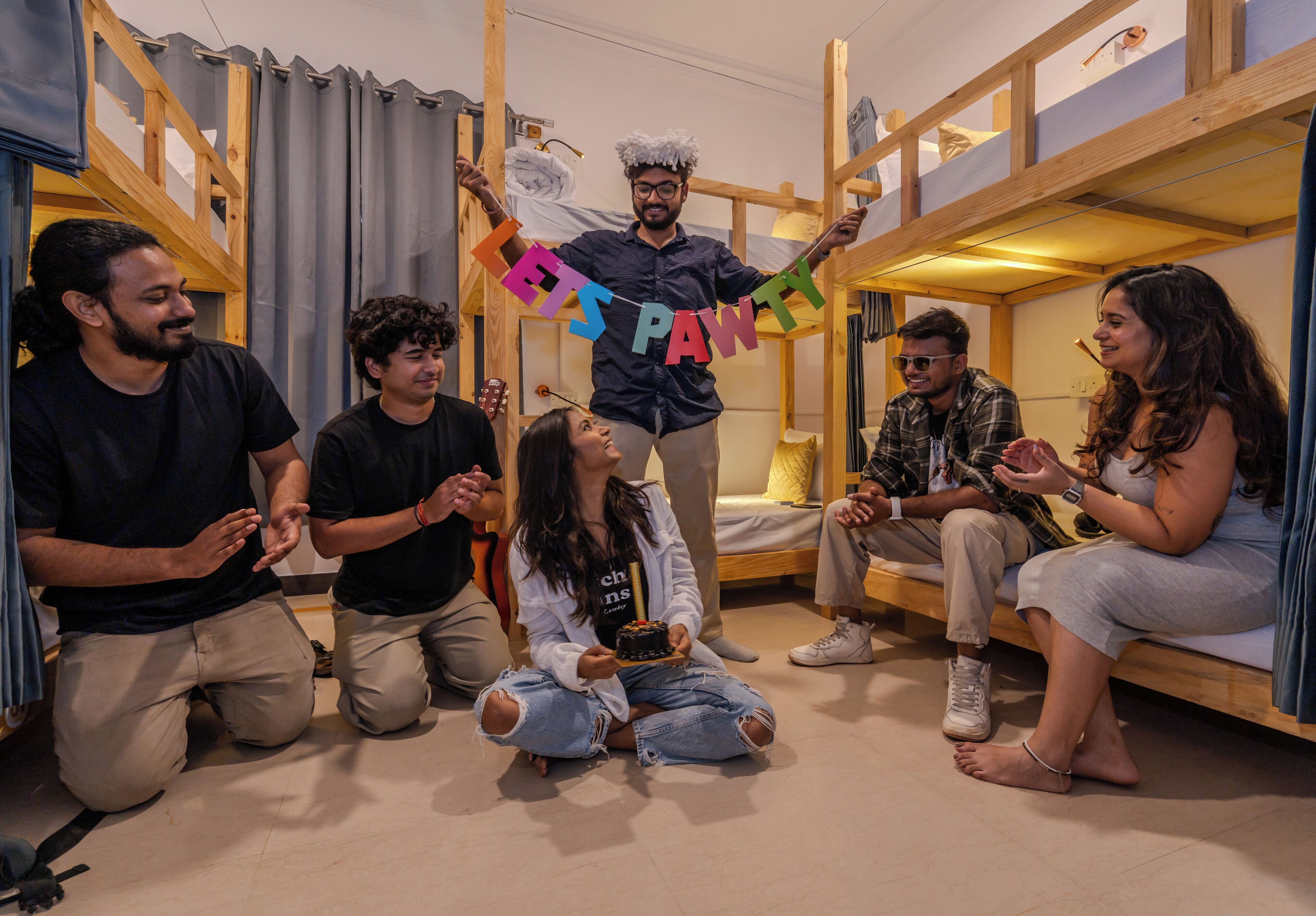A group of people in a room with bunk beds, wooden beams, and a curtain.