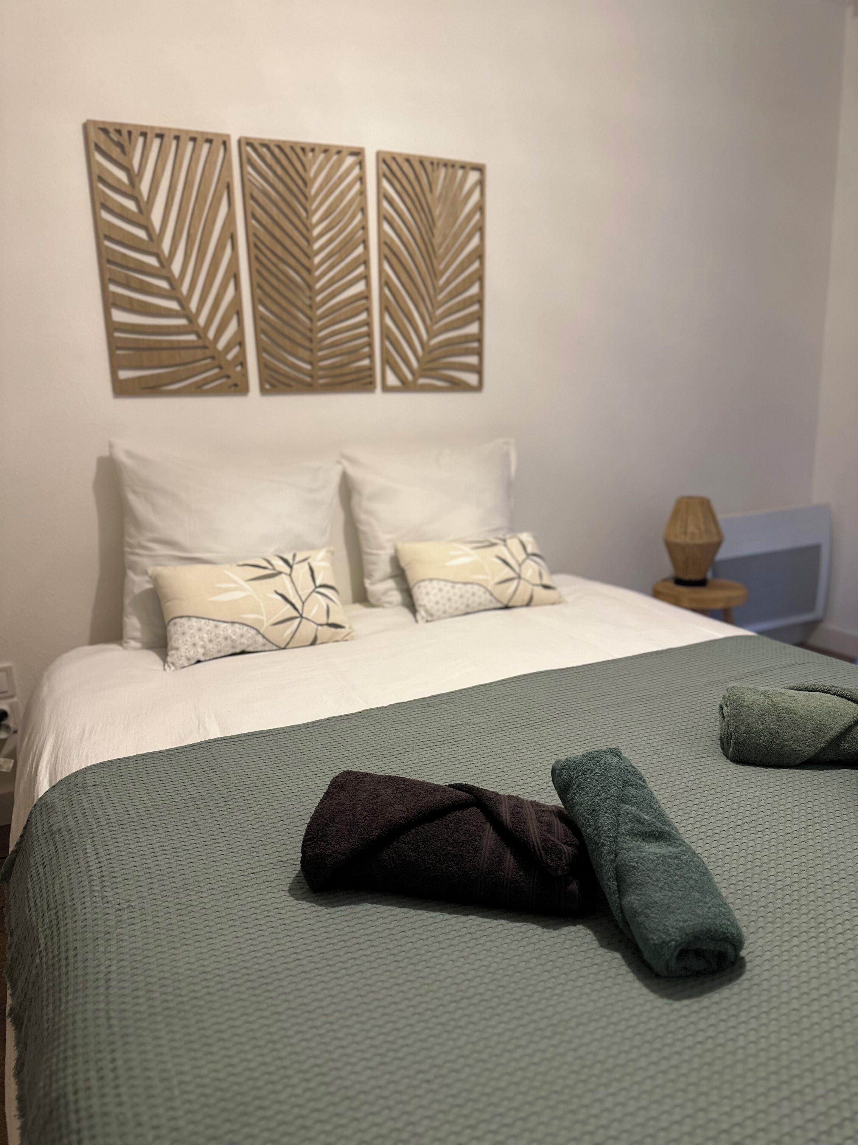 Un letto con una coperta verde a trama decorativa, due cuscini con motivo a foglie e due pannelli decorativi fissati alla parete.