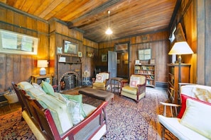 Quarto tradicional com paredes de madeira, lareira, conjunto de sofás e estante de livros.