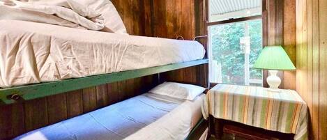 A bunk bed room with a window and a small table with a lamp.