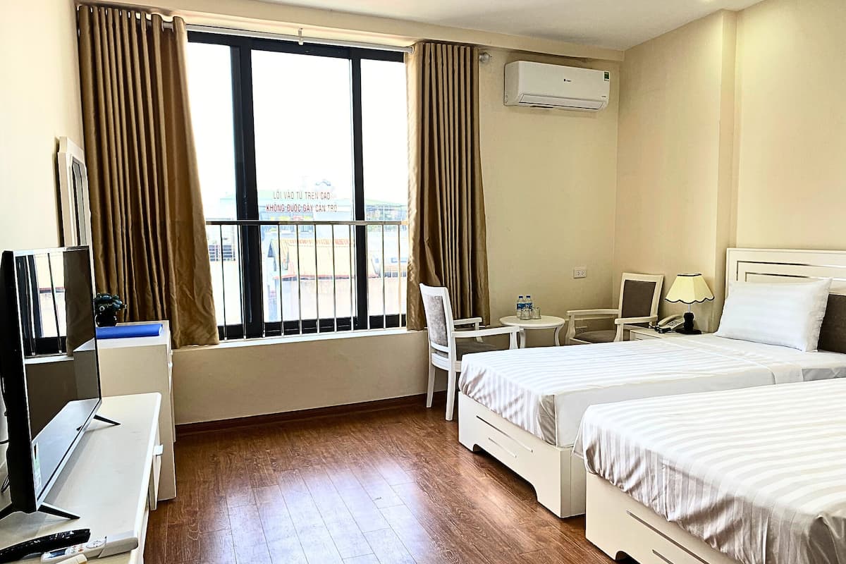 Una habitació d'hotel amb dos llits, un escriptori amb un ordinador, una cadira, una taula petita amb una làmpada i un aparell d'aire condicionat.