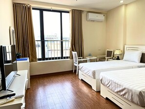 Hotelkamer met twee bedden, een bureau met computer, een stoel, een tafeltje met lamp en een airconditioning.