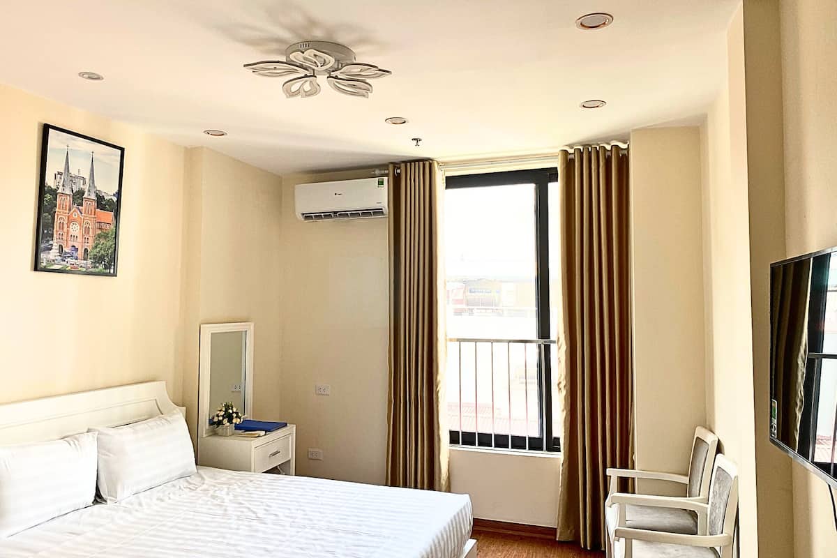 Habitació d'hotel amb llit, escriptori amb cadira, televisió, aire condicionat i finestra amb cortines.