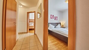 A hotel room with a wooden floor, a bed with white bedding, a nightstand with a lamp, and a painting on the wall. - Apartment Iglsberg Top 10 (Saalbach)