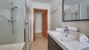 A modern bathroom with a glass-enclosed shower, a white sink with a mirror, and a wooden door leading to another room. - Apartment Iglsberg Top 10 (Saalbach)