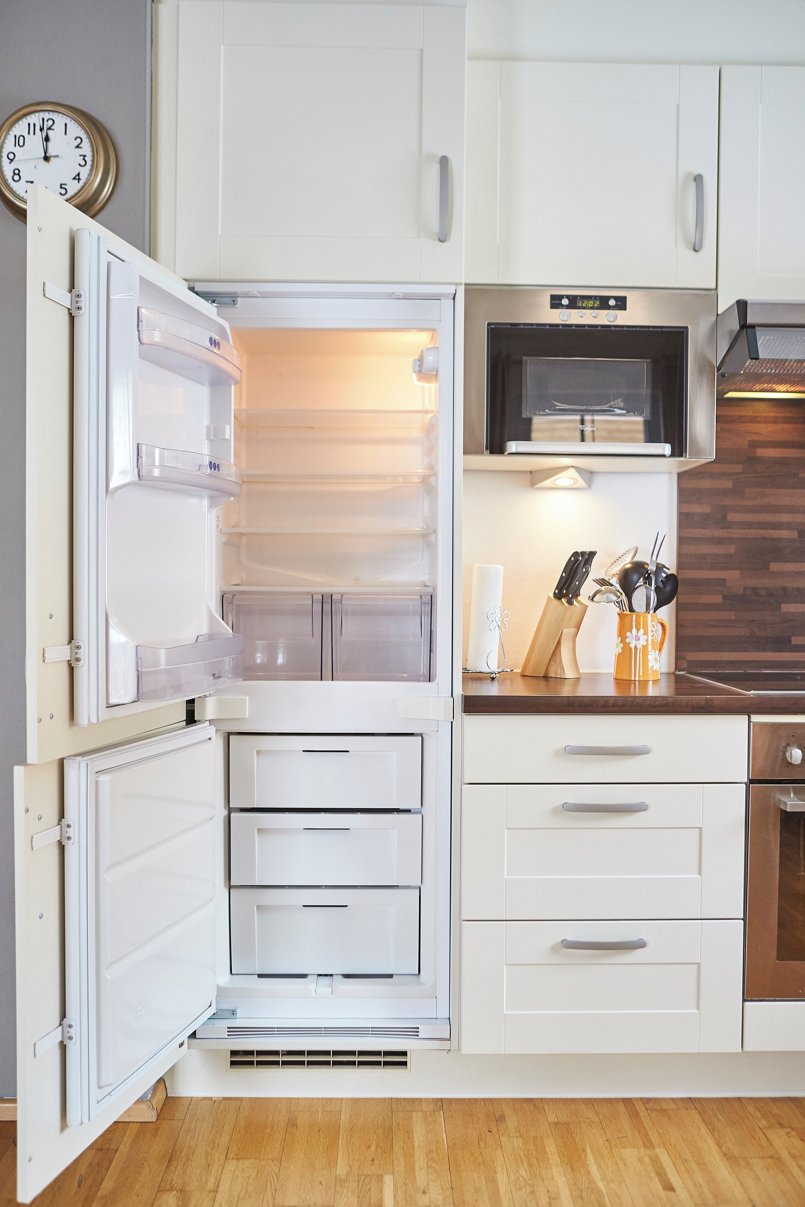 A kitchen with an open refrigerator, a microwave, and a wooden countertop with kitchen utensils.
