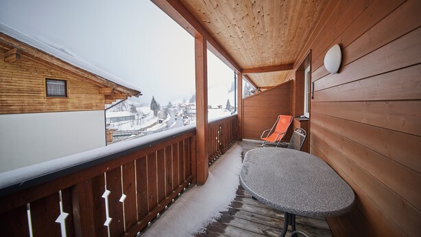 Un balcón de madera con una mesa y sillas, con vistas a un paisaje nevado.