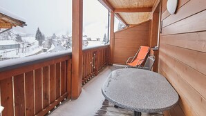 A wooden balcony with a table and chairs, snow on the floor, and a view of a snowy landscape. - Apartment Iglsberg Top 10 (Saalbach)