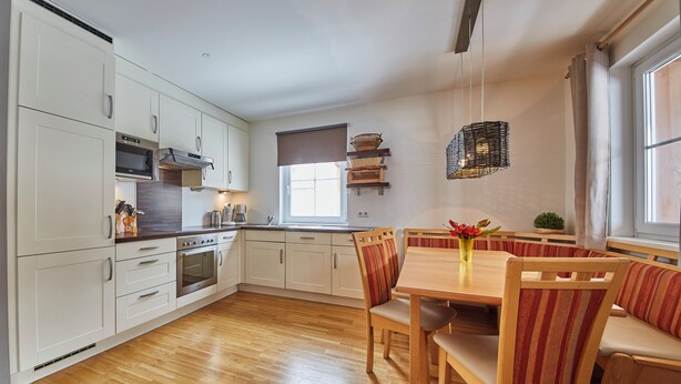 A modern kitchen with white cabinets, a wooden dining table, and striped chairs. - Apartment Iglsberg Top 10 (Saalbach)